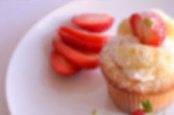 A cupcake with whipped frosting and fanned strawberries on a white plate