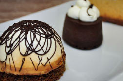 A domed dessert with chocolate lacing beside a small chocolate mousse cake